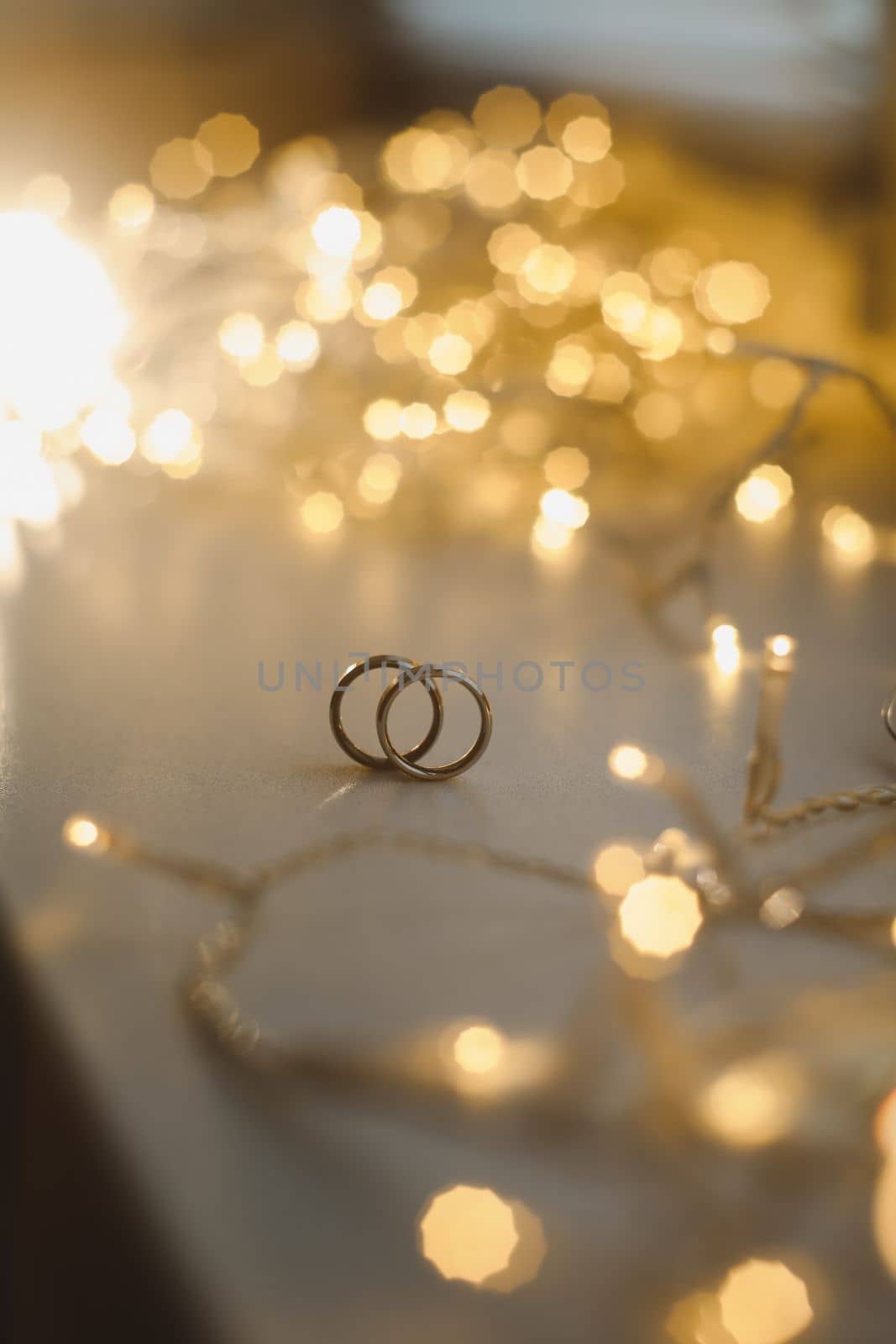 Wedding rings on blured bokeh glowing golden background. Symbol of love and romance on a textured glitter background with copy space for your greeting or congratulations.