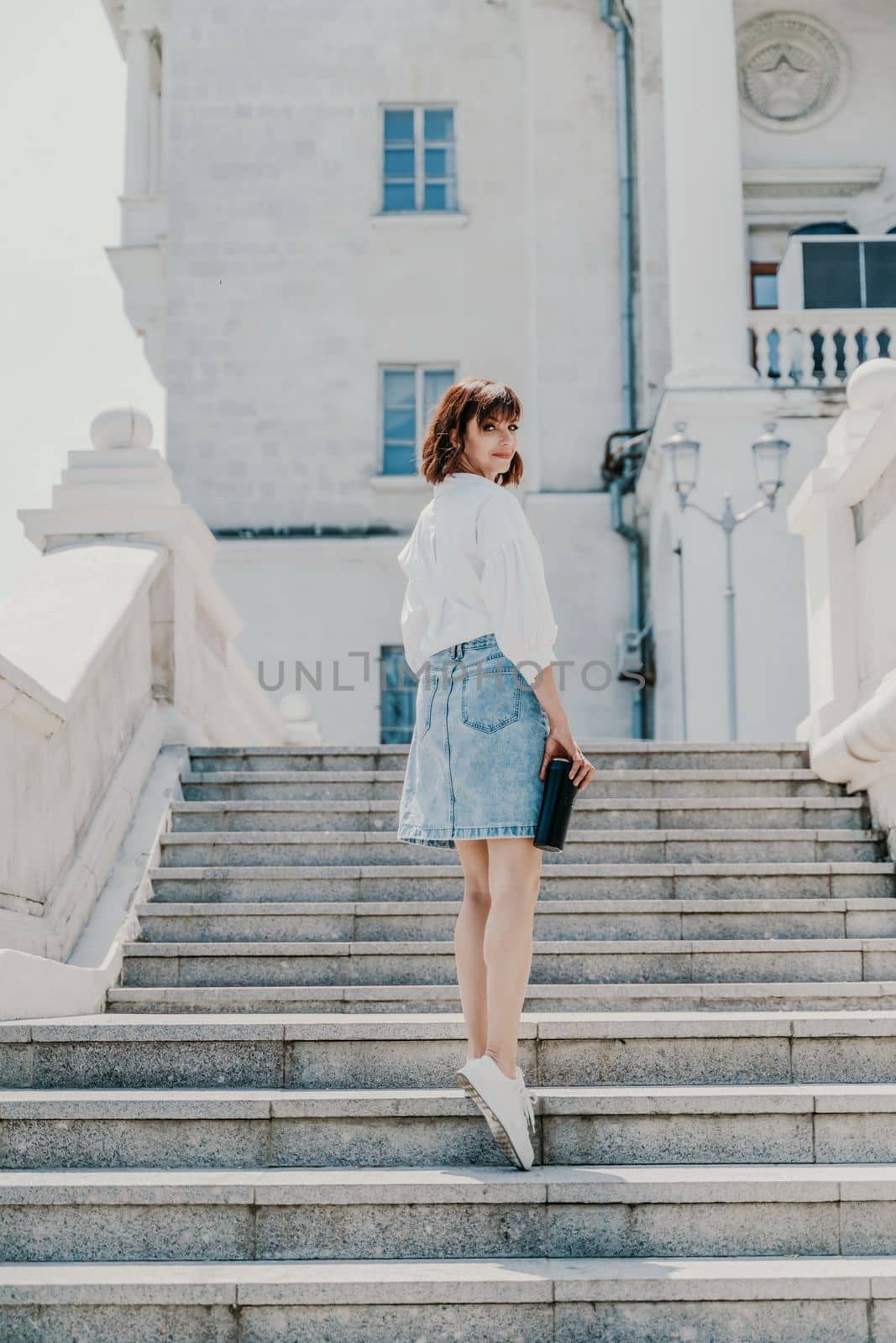 Woman staircase city. A business woman in a white shirt and denim skirt walks down the steps of an ancient building in the city by Matiunina