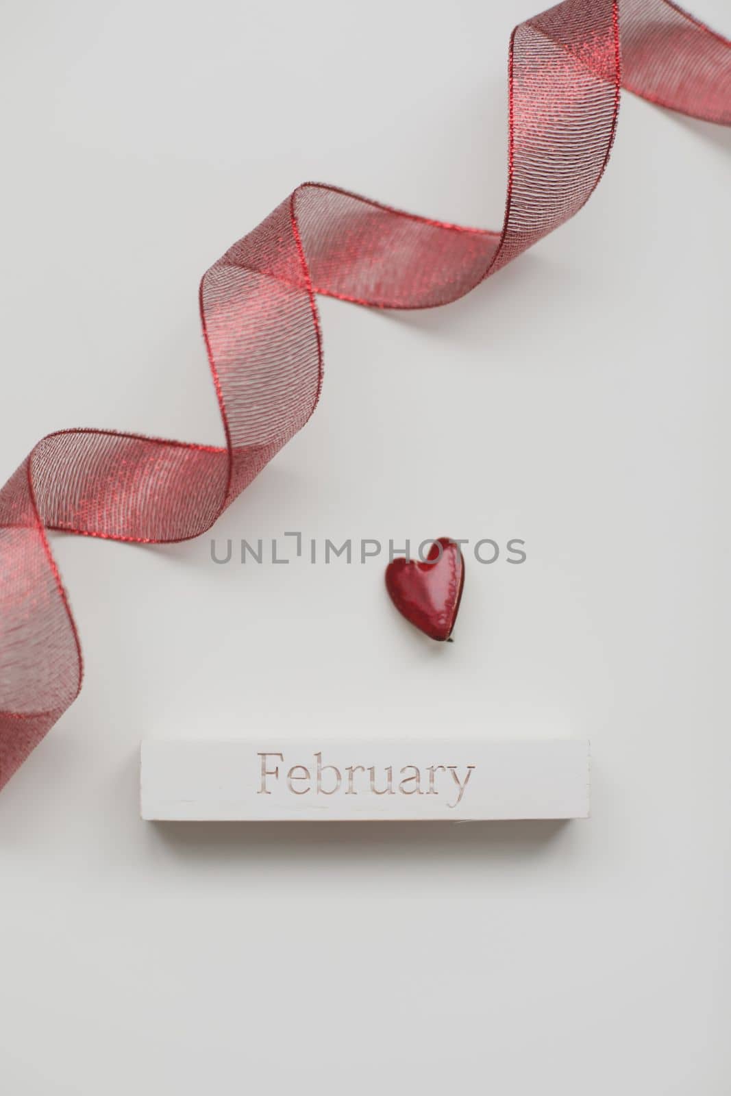 Greeting card with word February. Red ribbon and heart on white wooden background, flat lay.