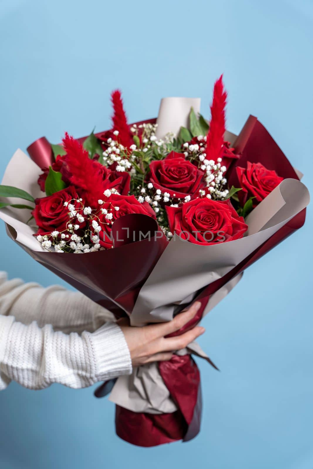 a beautiful bouquet of fresh red roses in women's hands on a light blue background. Congratulations on Mother's Day. valentine's day. wedding. vertycal photo