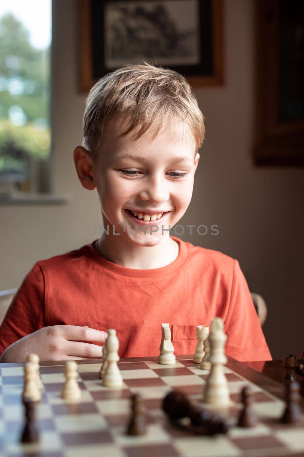 Young white child playing a game of chess on large chess board. Chess board on table in front of school boy thinking of next move by Len44ik