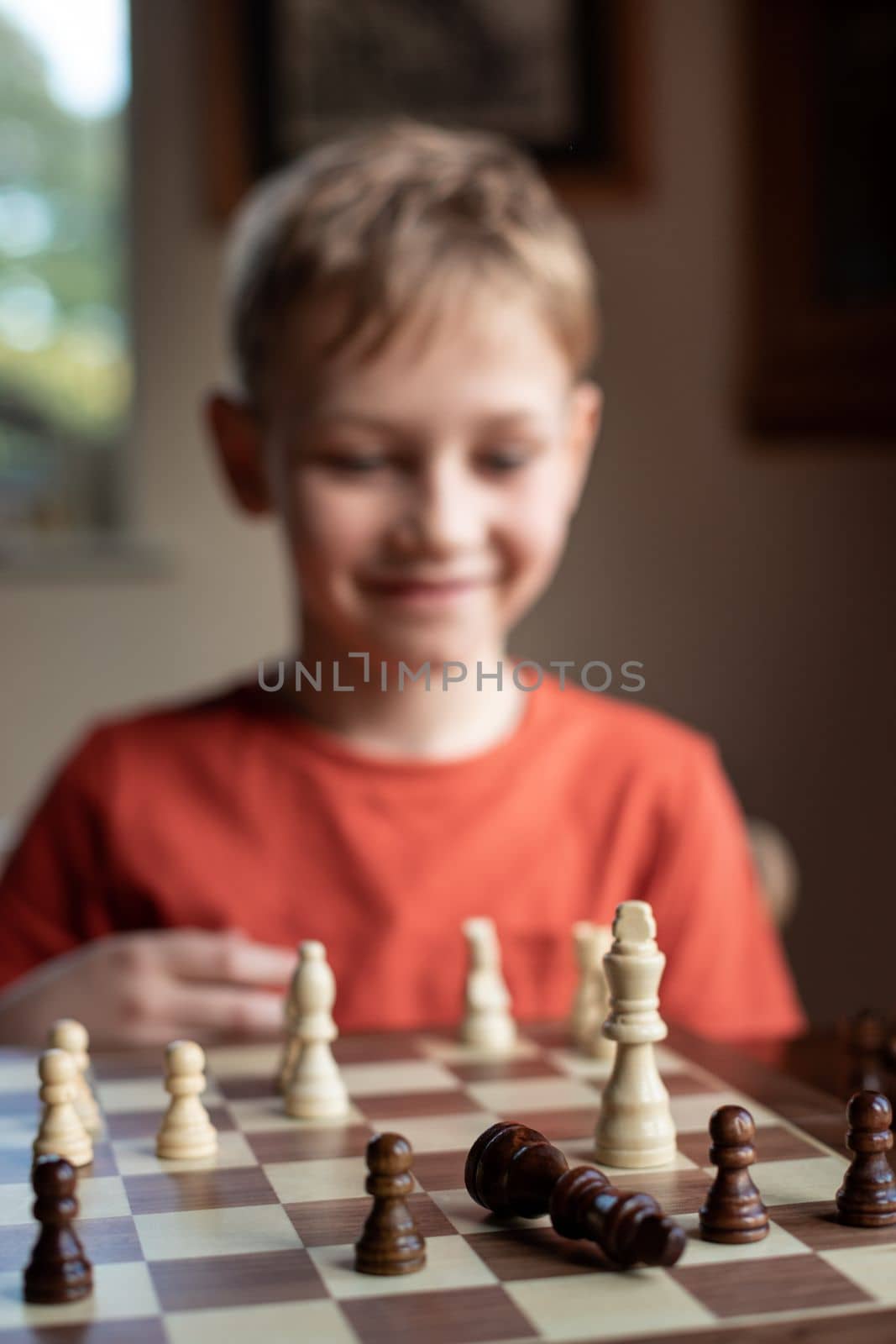 Young white child playing a game of chess on large chess board. Chess board on table in front of school boy thinking of next move by Len44ik