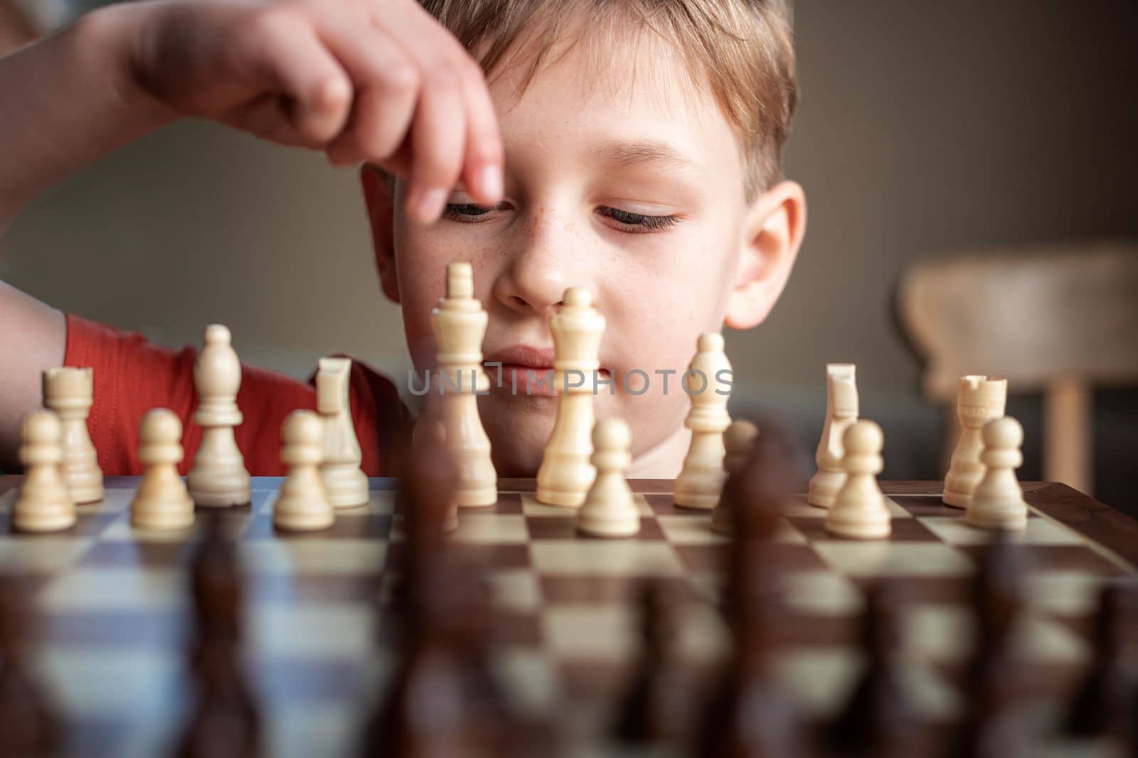Young white child playing a game of chess on large chess board. Chess board on table in front of school boy thinking of next move by Len44ik