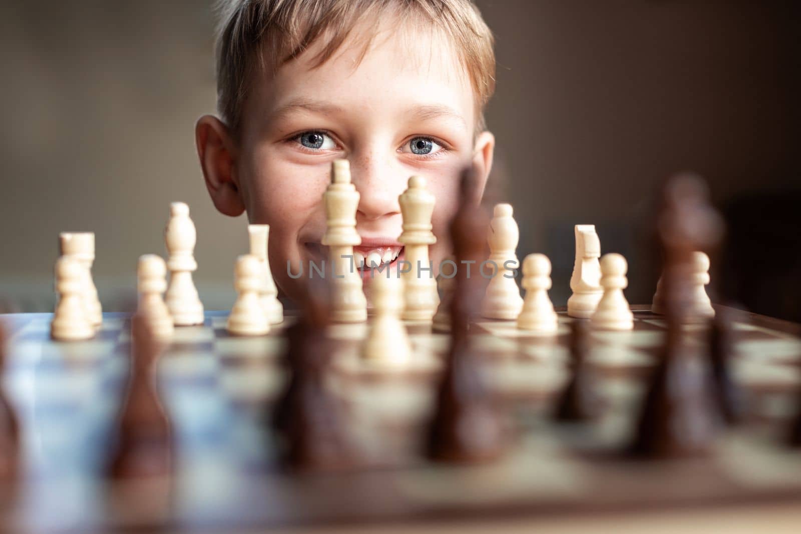Young white child playing a game of chess on large chess board. Chess board on table in front of school boy thinking of next move, tournament
