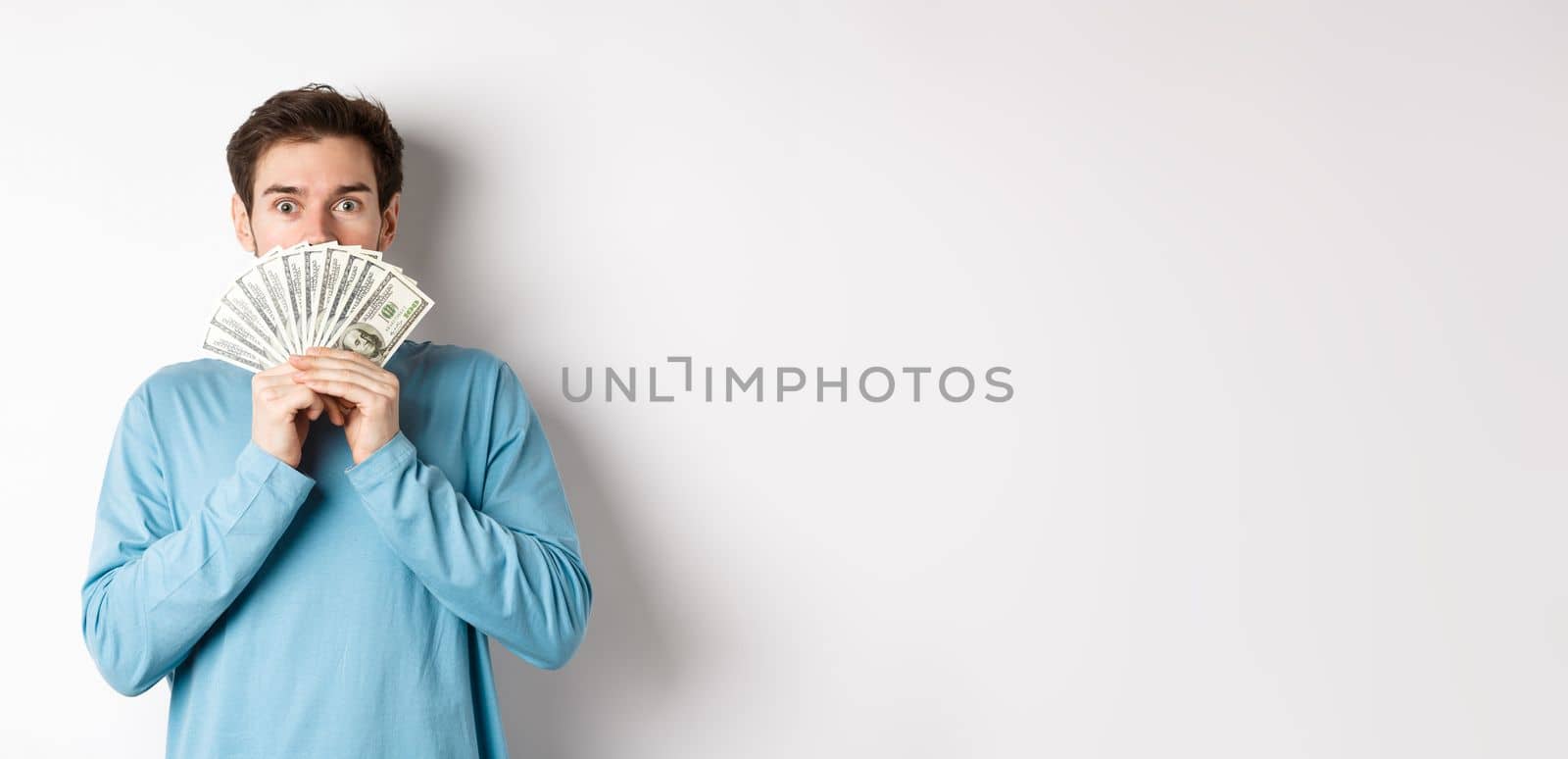 Surprised and amazed handsome guy showing money, looking at promo offer, going shopping with cash, standing over white background by Benzoix