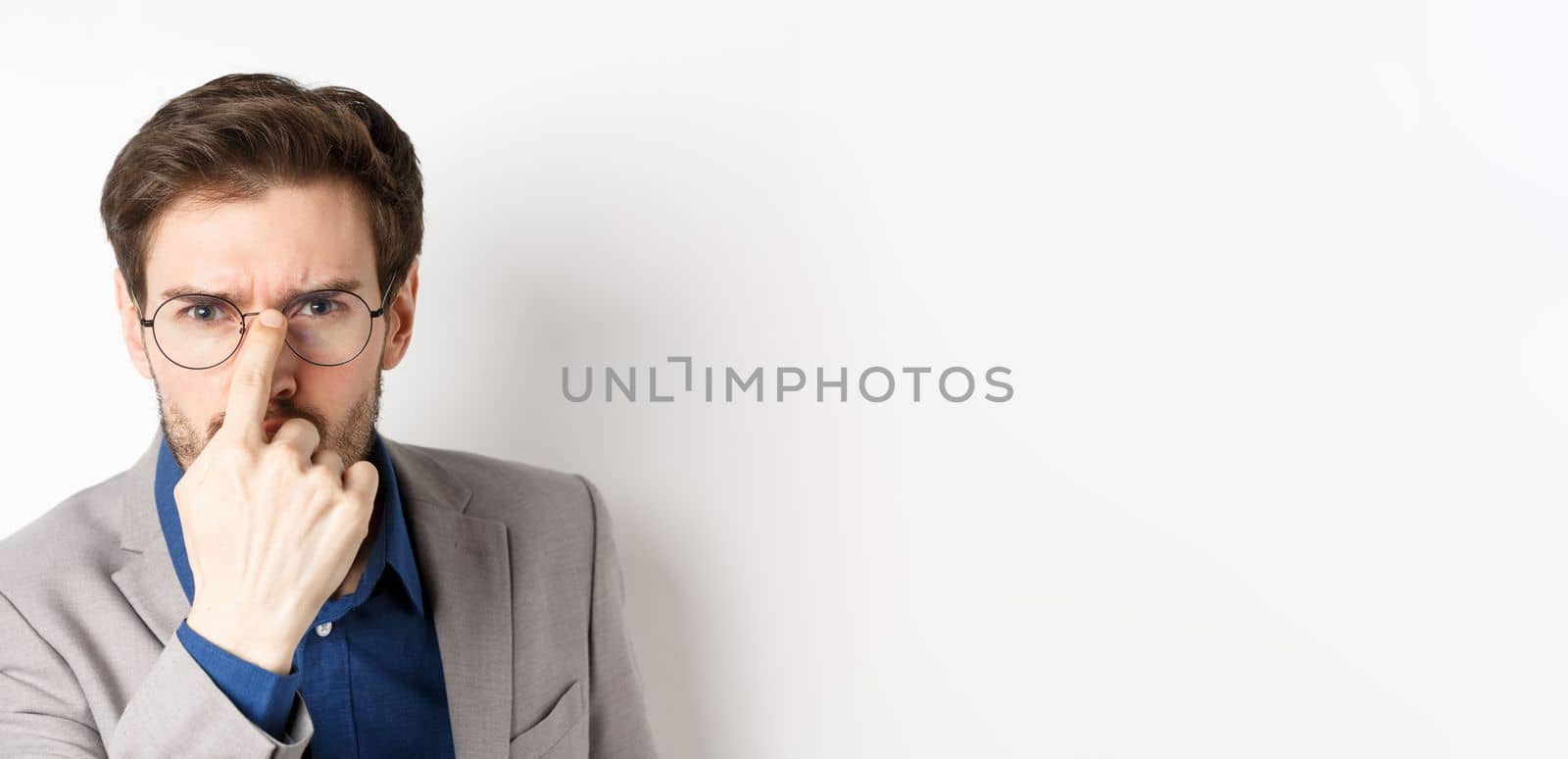 Serious boss in suit frowning, put on glasses and looking suspicious at camera, white background by Benzoix