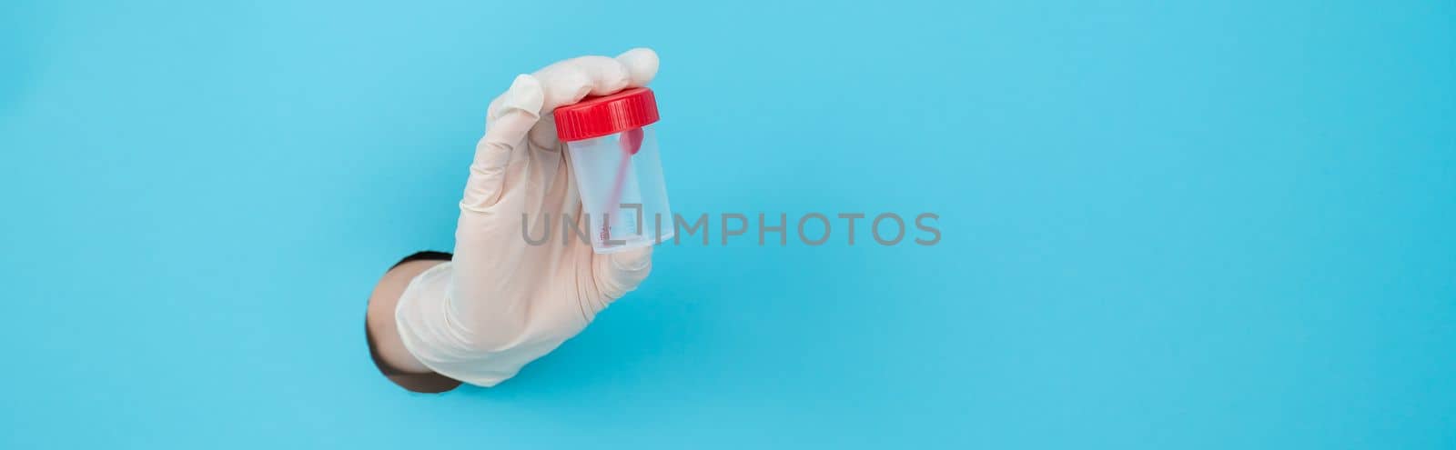 A woman's hand in a rubber glove sticks out through a blue paper background and holds a container for collecting feces