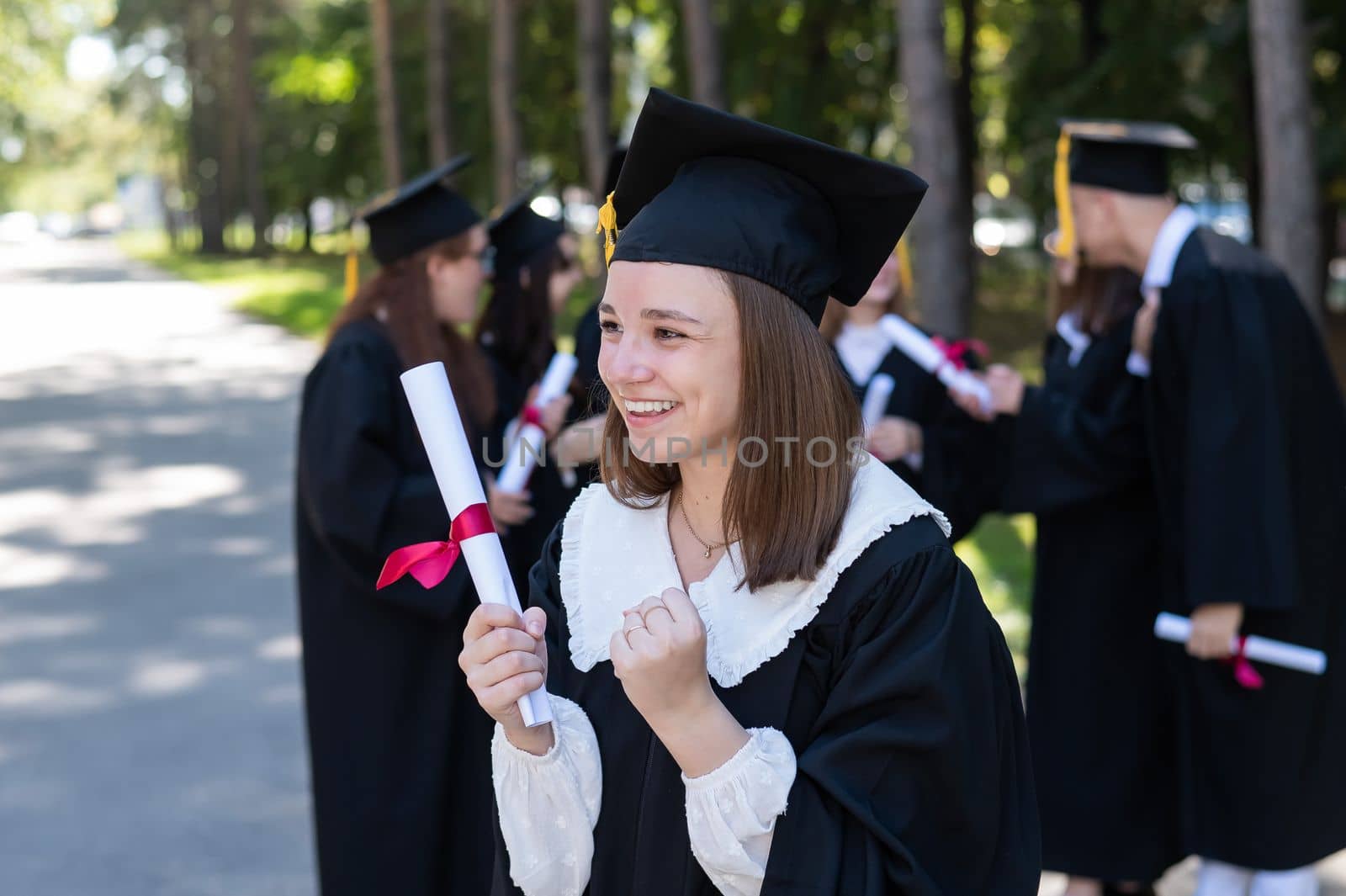 Group of happy students in graduation gowns outdoors. A young girl is happy to receive her diploma. by mrwed54