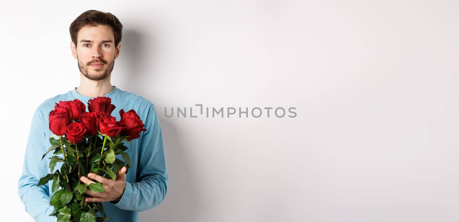 Confident young man bring flowers on Valentines day date, holding romantic bouquet, standing over white background.