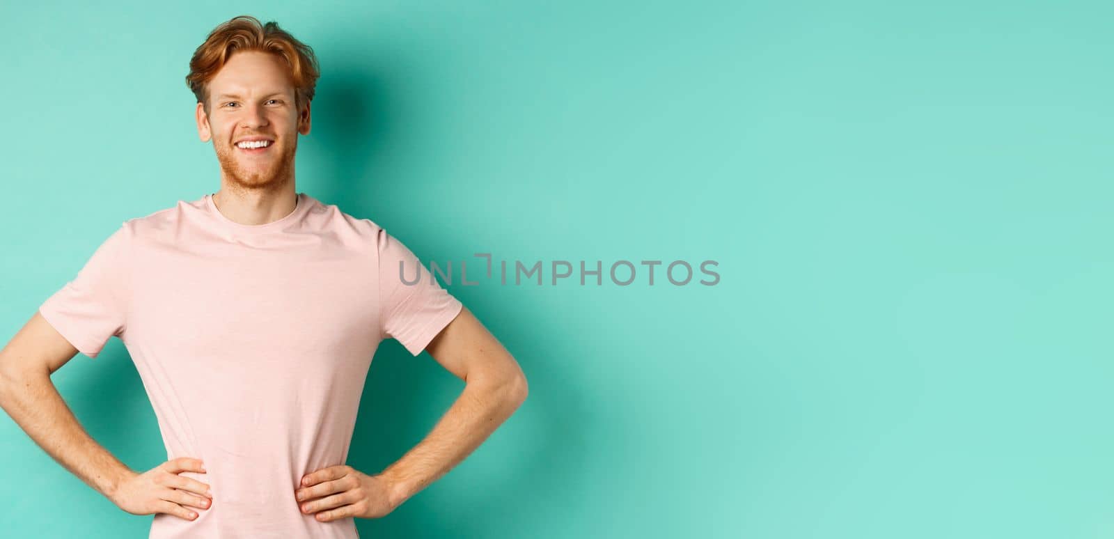 Enthusiastic young man with red hair, wearing t-shirt, standing happy and proud with hands on hops, standing over turquoise background by Benzoix