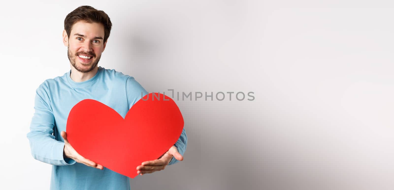 Happy gay man giving big red heart to his lover on valentines day, concept of romantic date and love celebration, standing over white background.