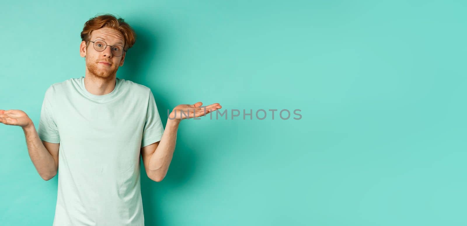 Portrait of confused redhead man in t-shirt and glasses know nothing, shrugging shoulders and looking clueless at camera, standing against turquoise background by Benzoix