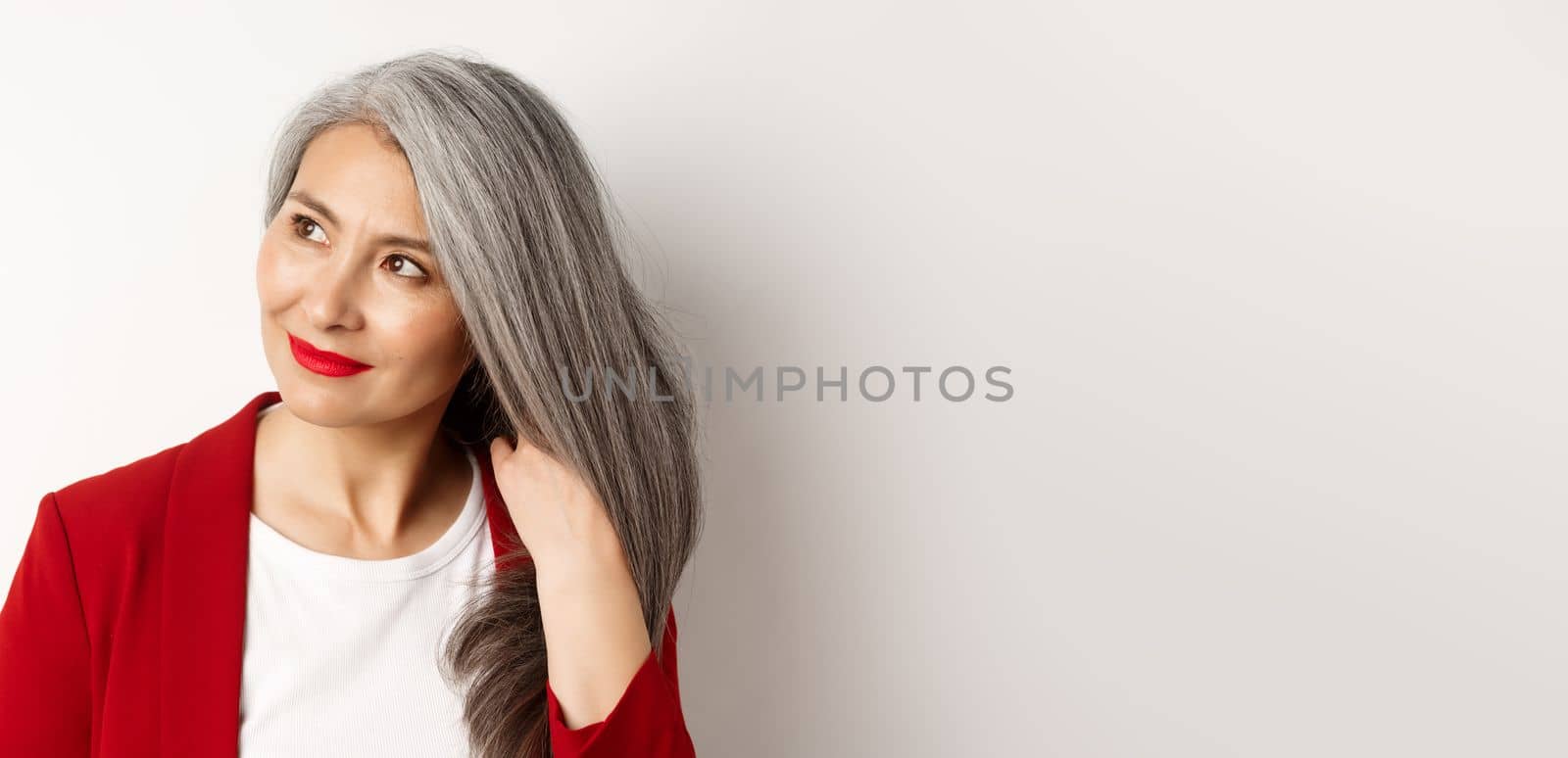 Beauty and haircare concept. Close up of elegant asian senior woman showing shiny and healthy grey hair, smiling and looking aside, white background by Benzoix
