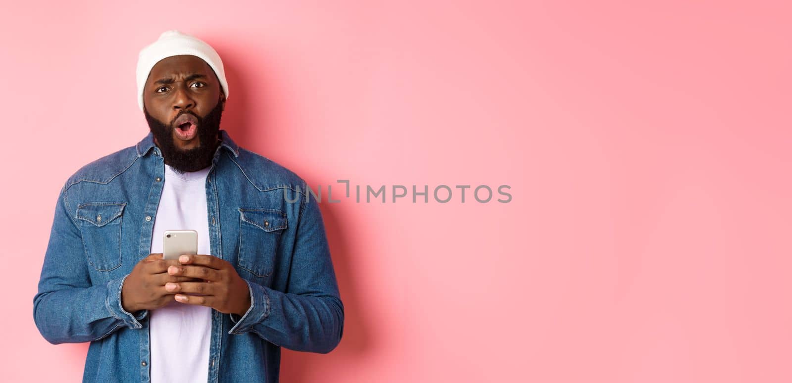 Technology and online shopping concept. Confused and disappointed african-american man complaining, holding mobile phone and staring at camera by Benzoix