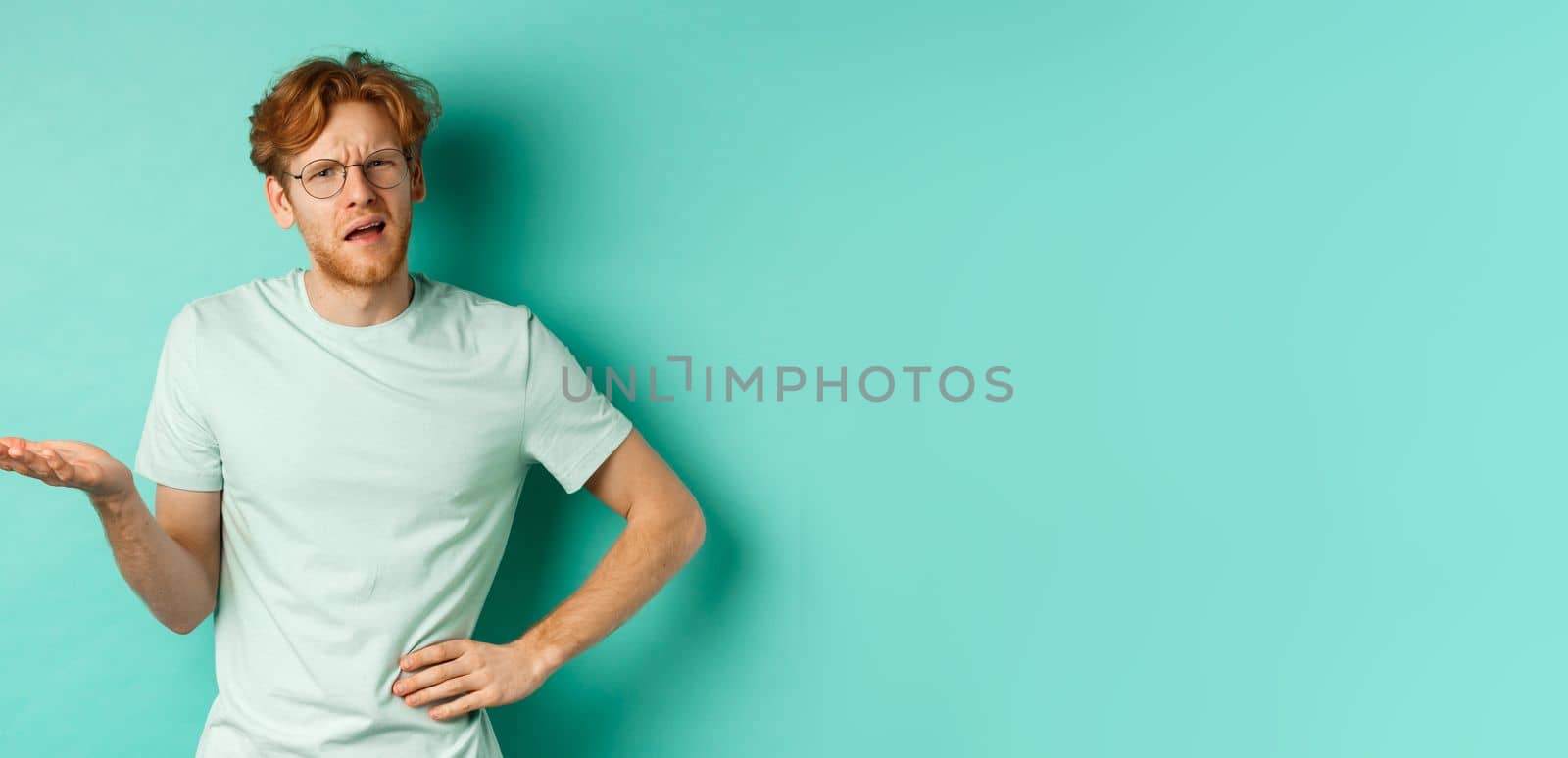 Confused redhead man trying to understand something, squinting clueless and stretch out one hand, looking puzzled, standing over mint background by Benzoix