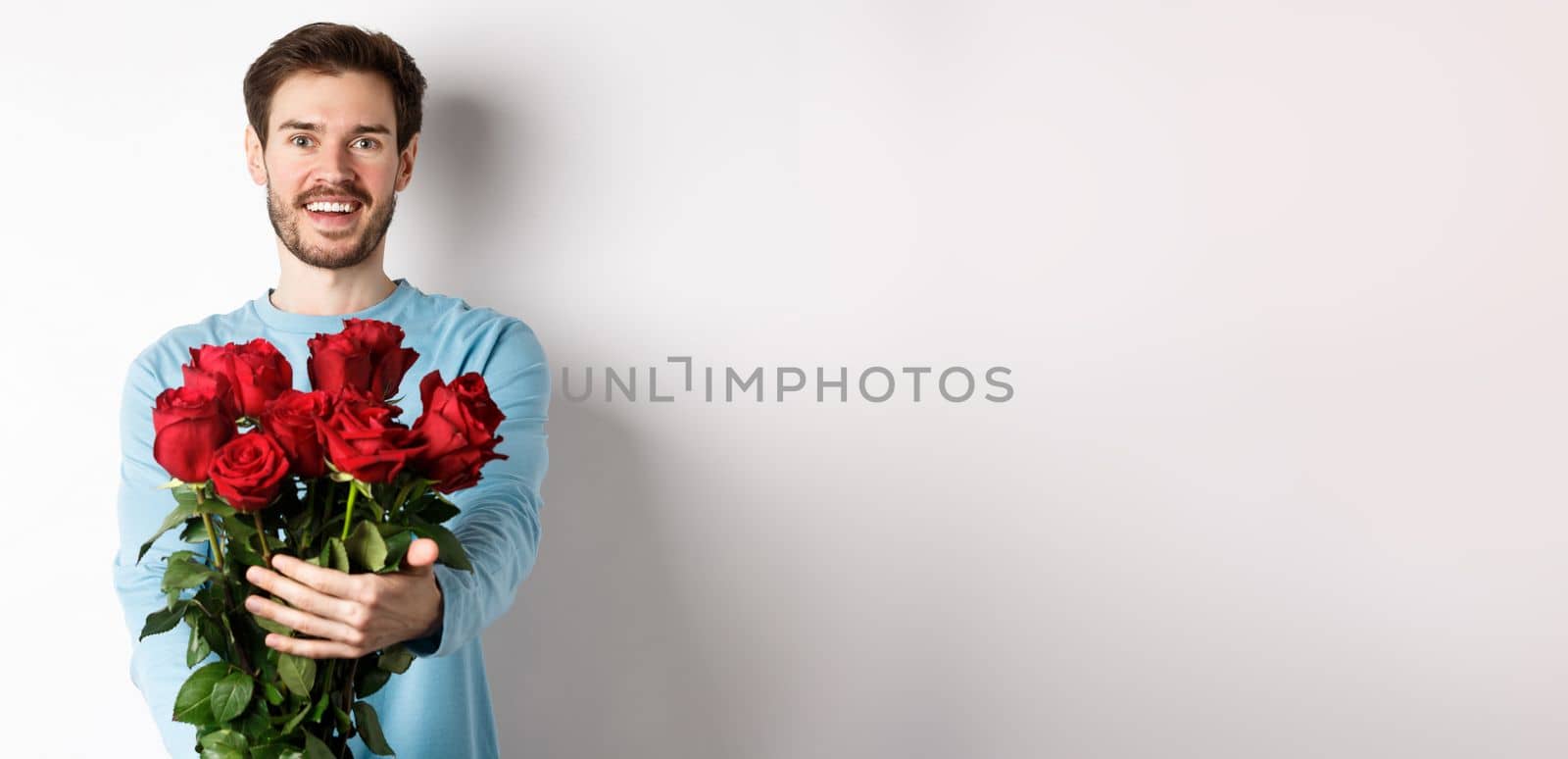 Handsome bearded guy stretch out hands, giving bouquet of roses and smiling, bring flowers on romantic date, celebrating Valentines day with lover, standing over white background by Benzoix