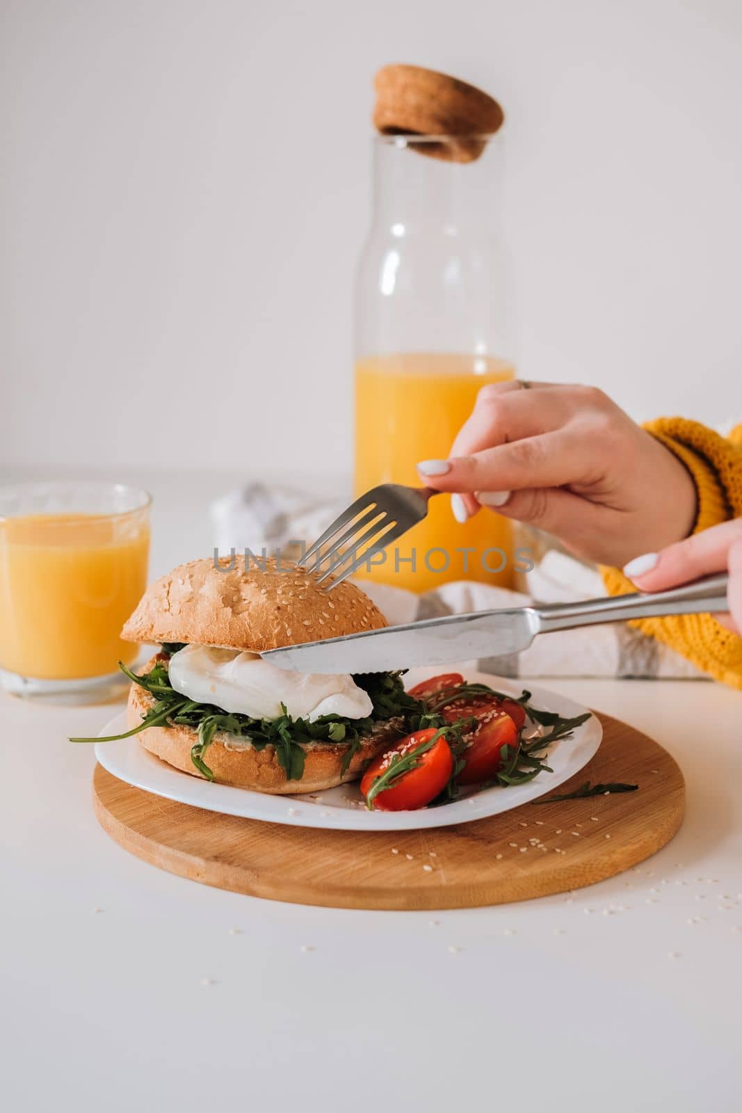 Breakfast sandwich with egg and arugula and cherry tomatoes on table with orange juice