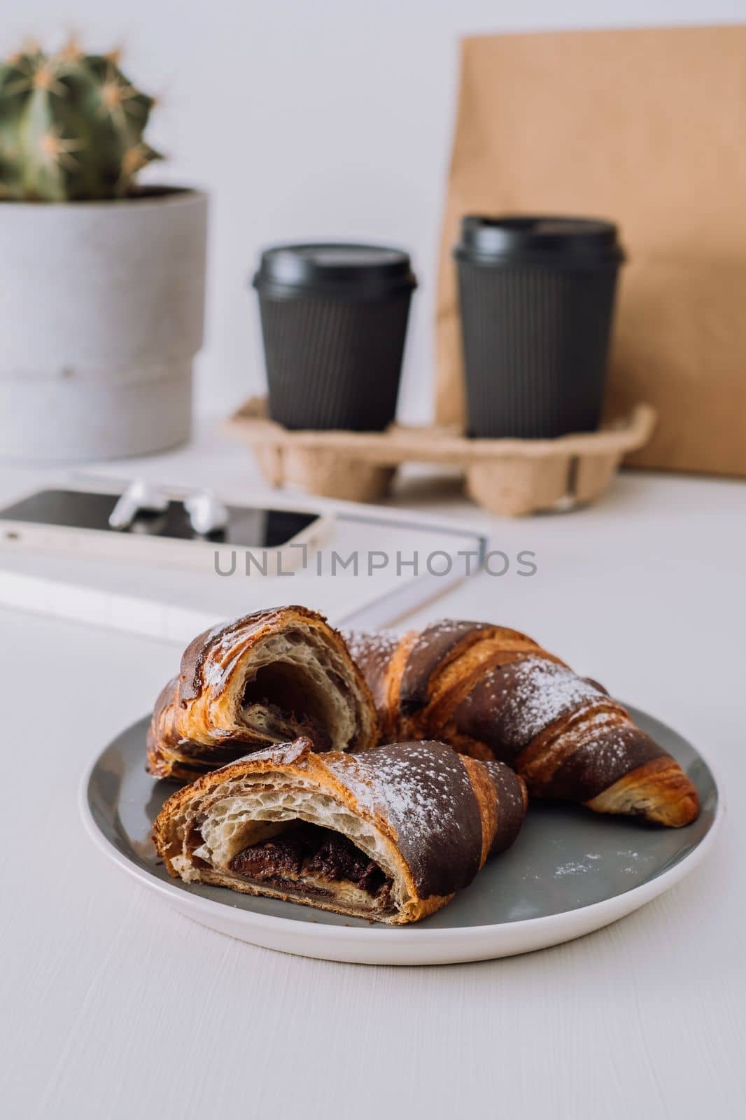 Close up of chocolate croissants with cups of coffee and notepad with smartphone on background, food delivery concept