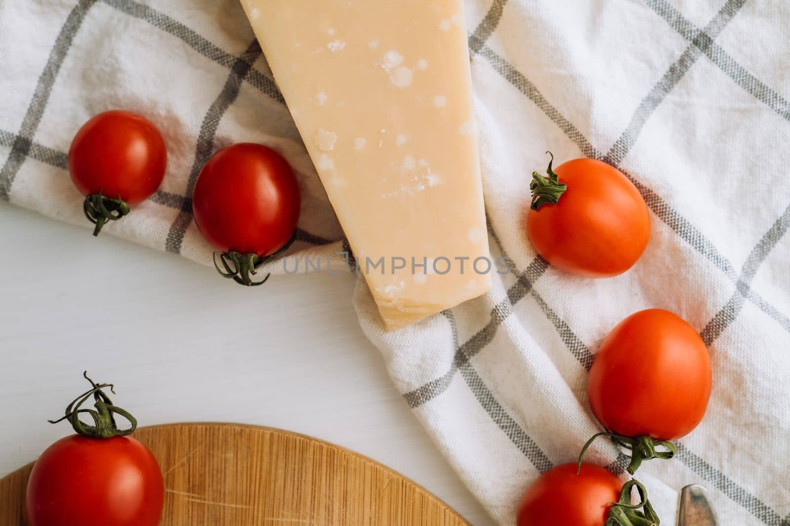 Cherry tomatoes and a piece of parmesan cheese on the table with a kitchen towel and a cutting board by Romvy