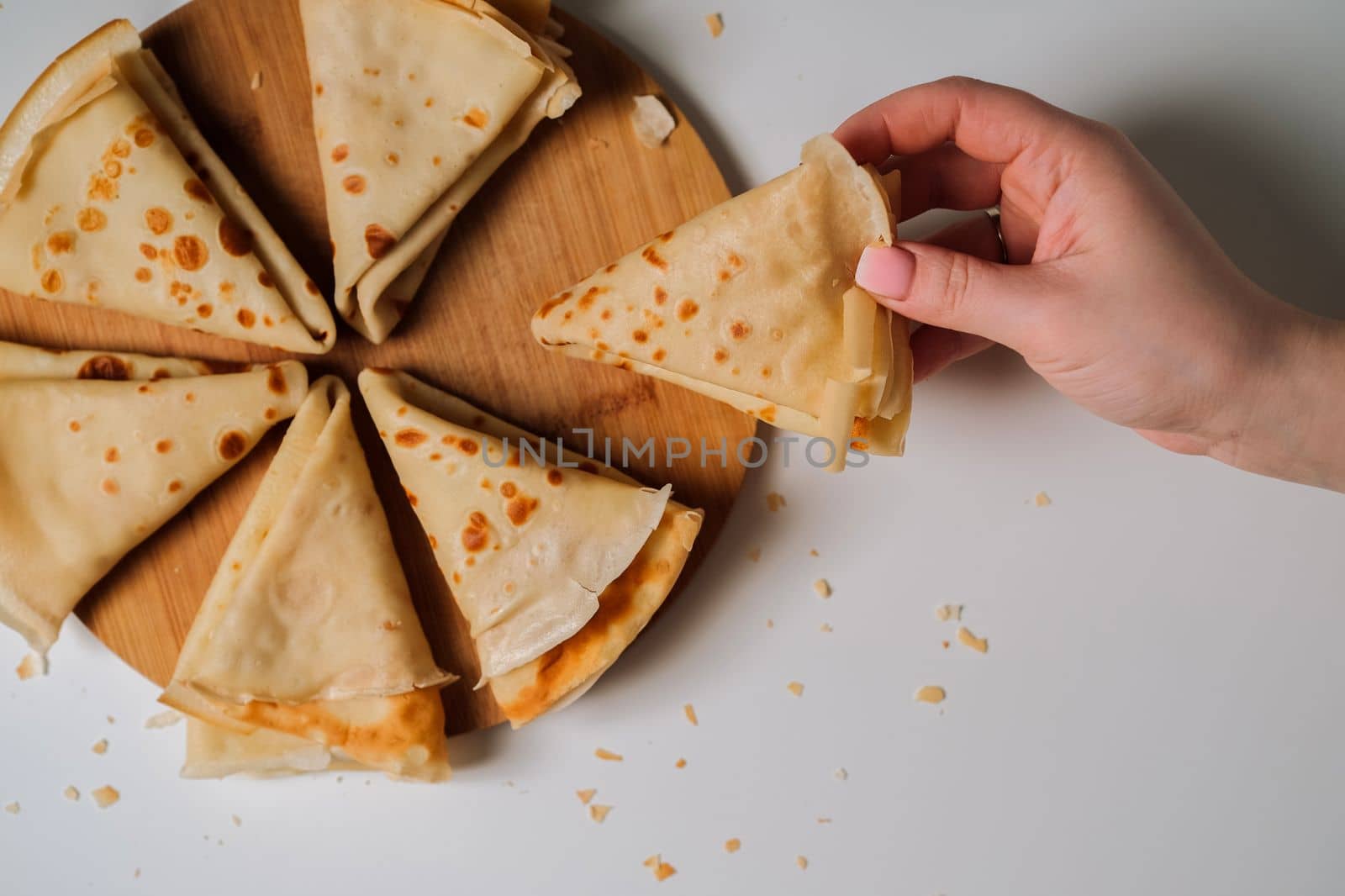Woman's hand holding delicious crepe, crepes laid out in triangles in a circle on wooden board, flat lay
