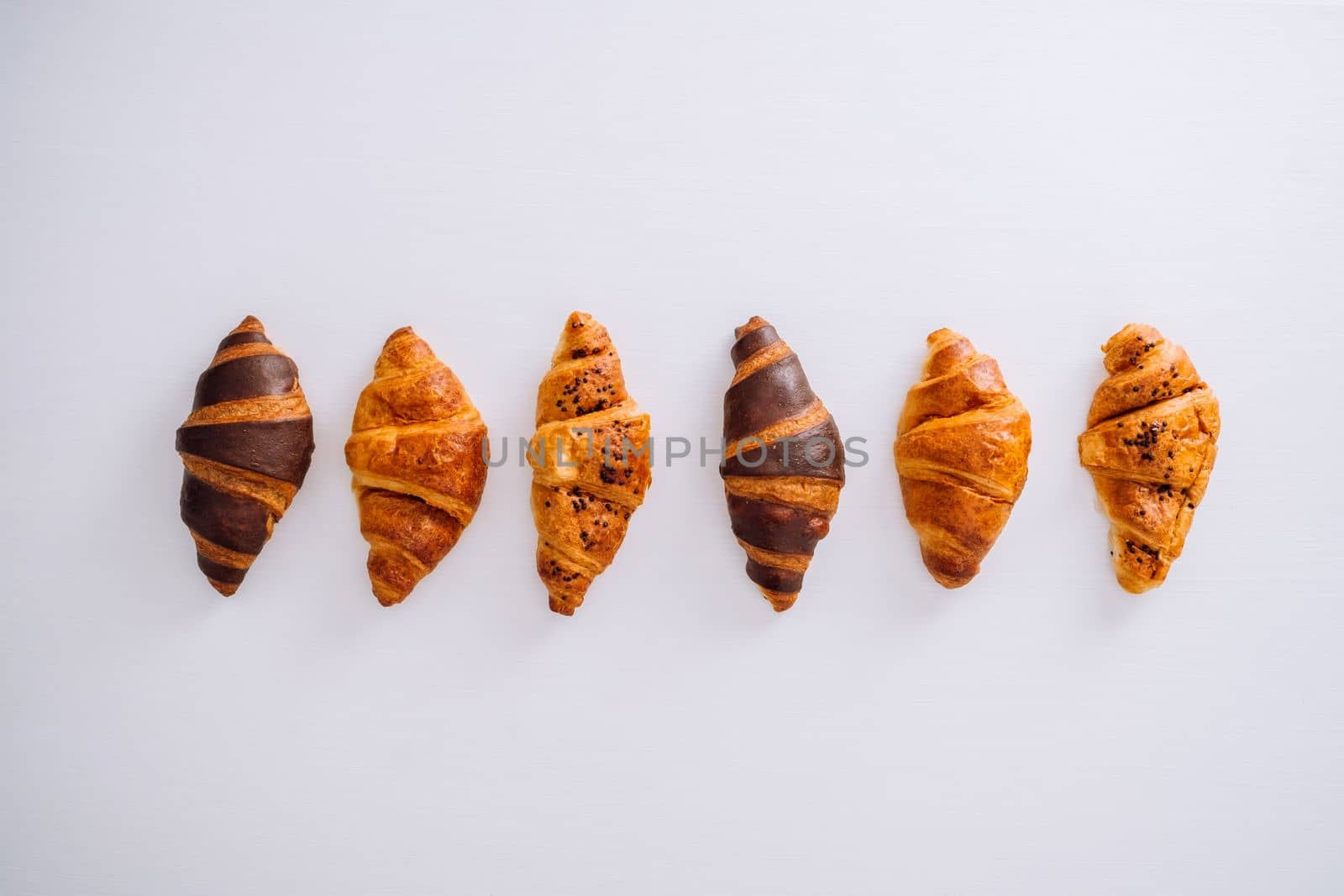 Flat lay of several delicious brown and chocolate croissants laid out in a line on a white table by Romvy