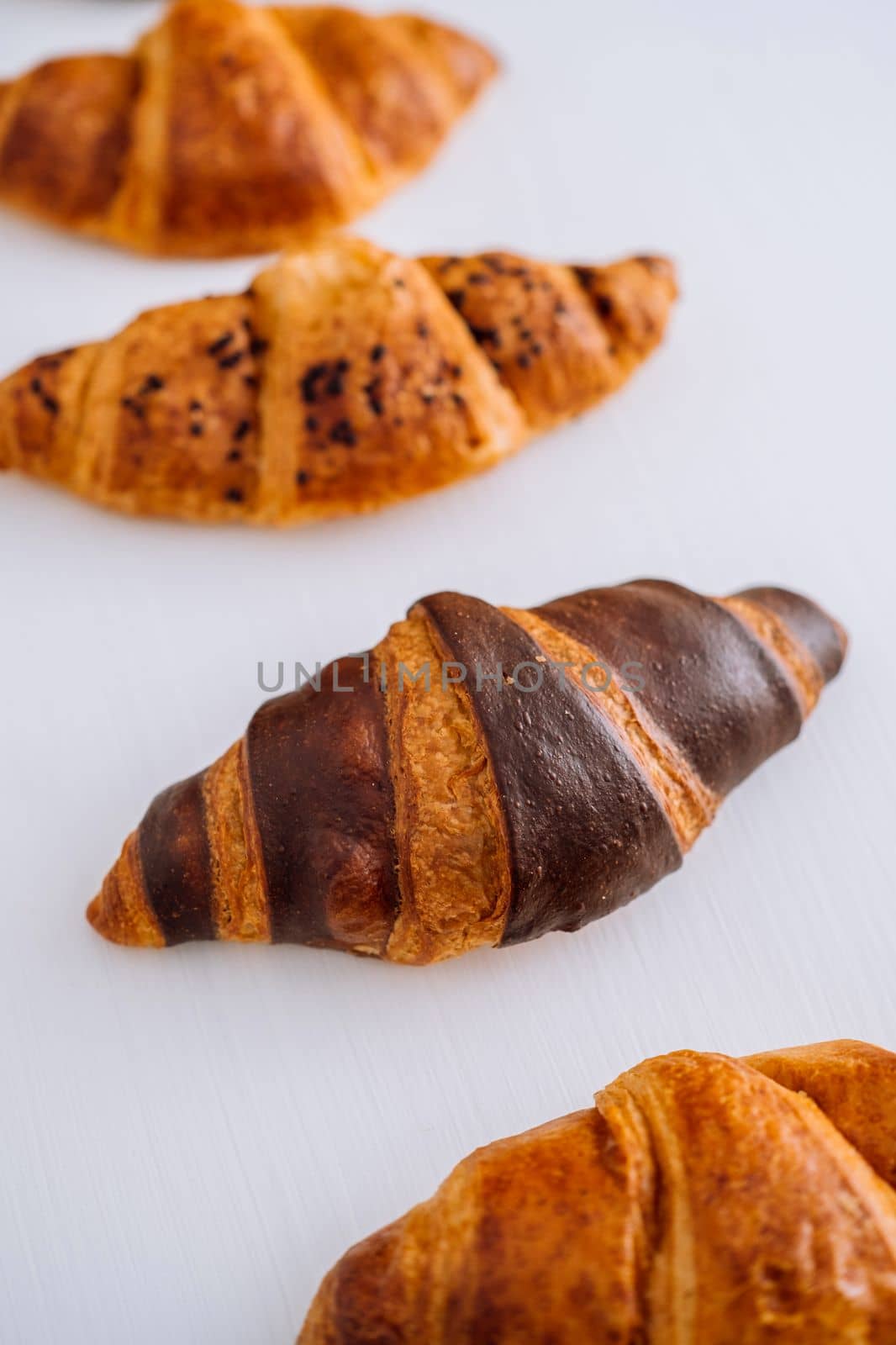 Close up of bunch of delicious brown and chocolate croissants laid out on white table