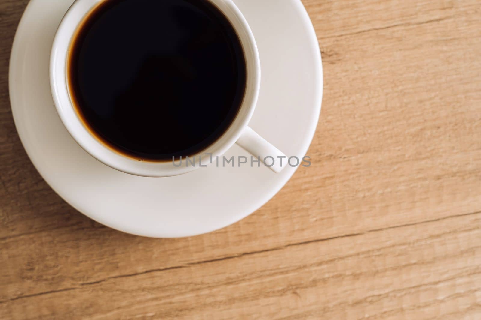 Flat lay cup of black coffee with a saucer on wooden table