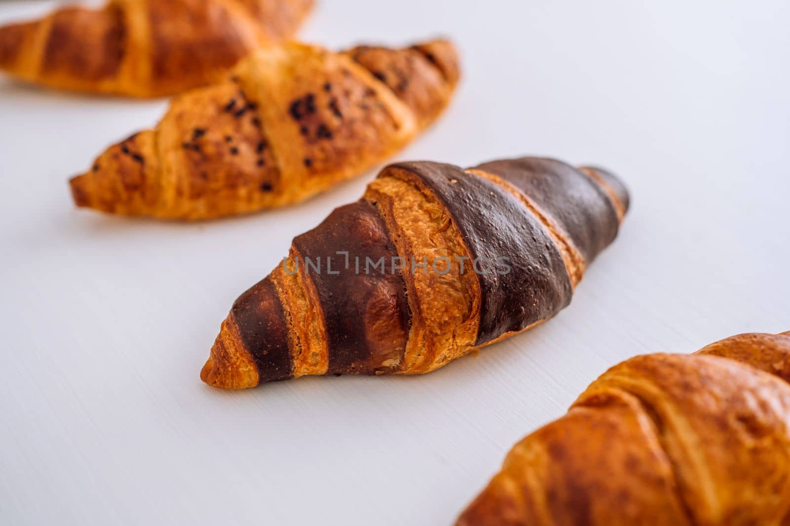 Close up of bunch of delicious brown and chocolate croissants laid out on white table
