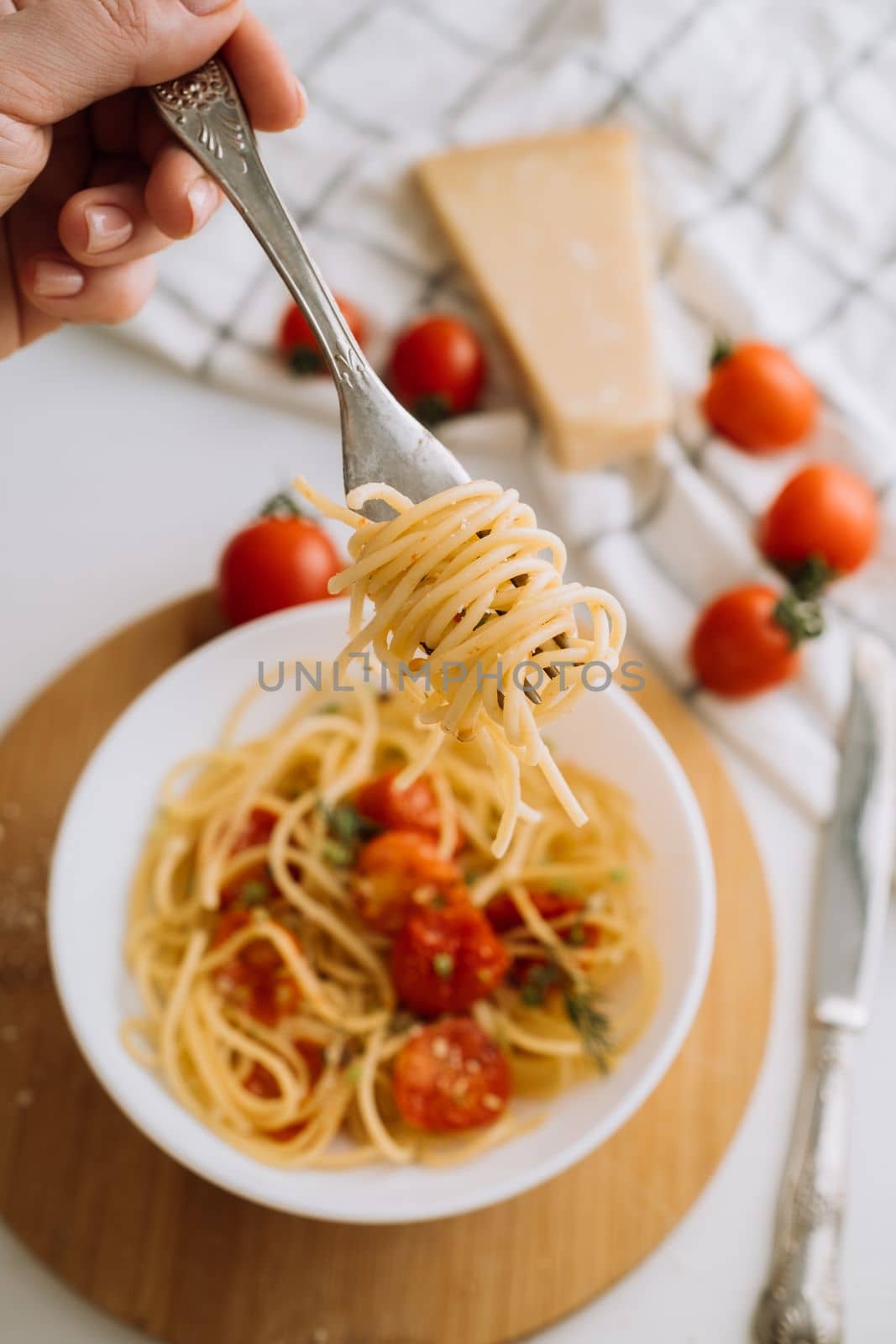 Spaghetti wrapped on fork in the background of a portion of pasta with cherry tomatoes in a plate and parmesan cheese
