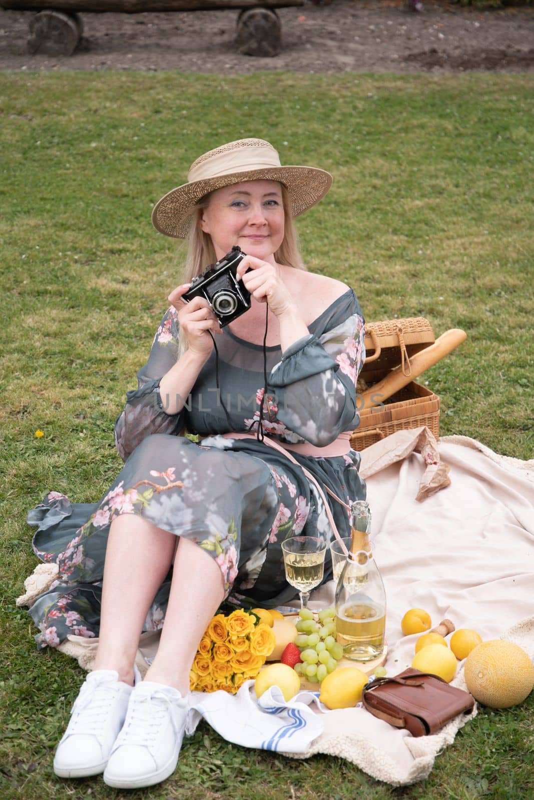 a young woman in a long dress and straw hat is resting on a picnic with fruits, cheese plate and champagne, rest from worries and household chores parks and recreation areas,.High quality photo