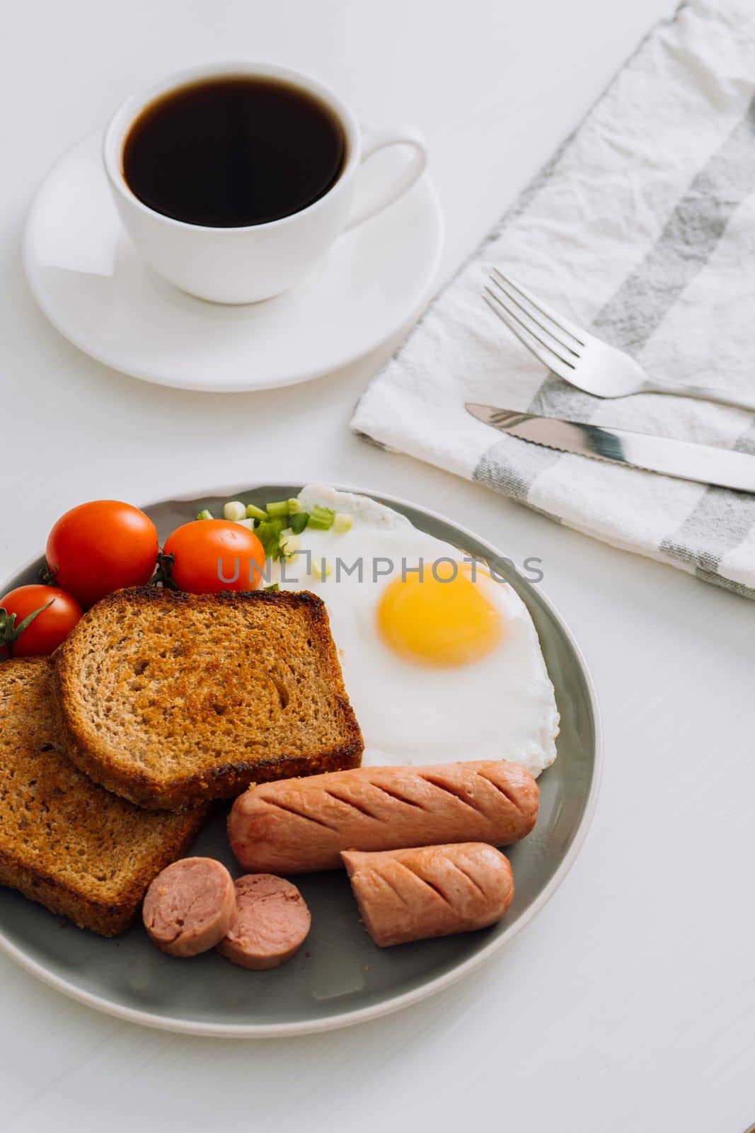 Breakfast plate with cup of black coffee, grilled sausage and whole wheat toast with fried egg and cherry tomatoes on plate