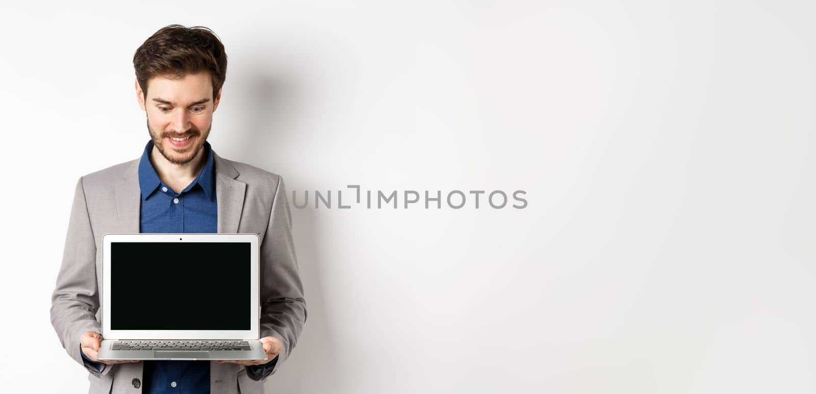 Handsome caucasian businessman in suit showing empty laptop screen, demonstrate promo, standing on white background by Benzoix