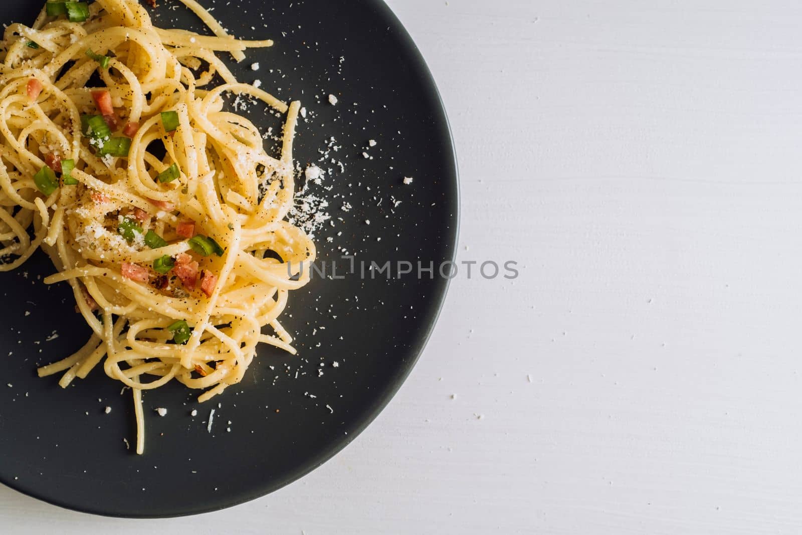 Close up spaghetti pasta sprinkled with cheese parmesan and green onions on black plate on a white table with copy space