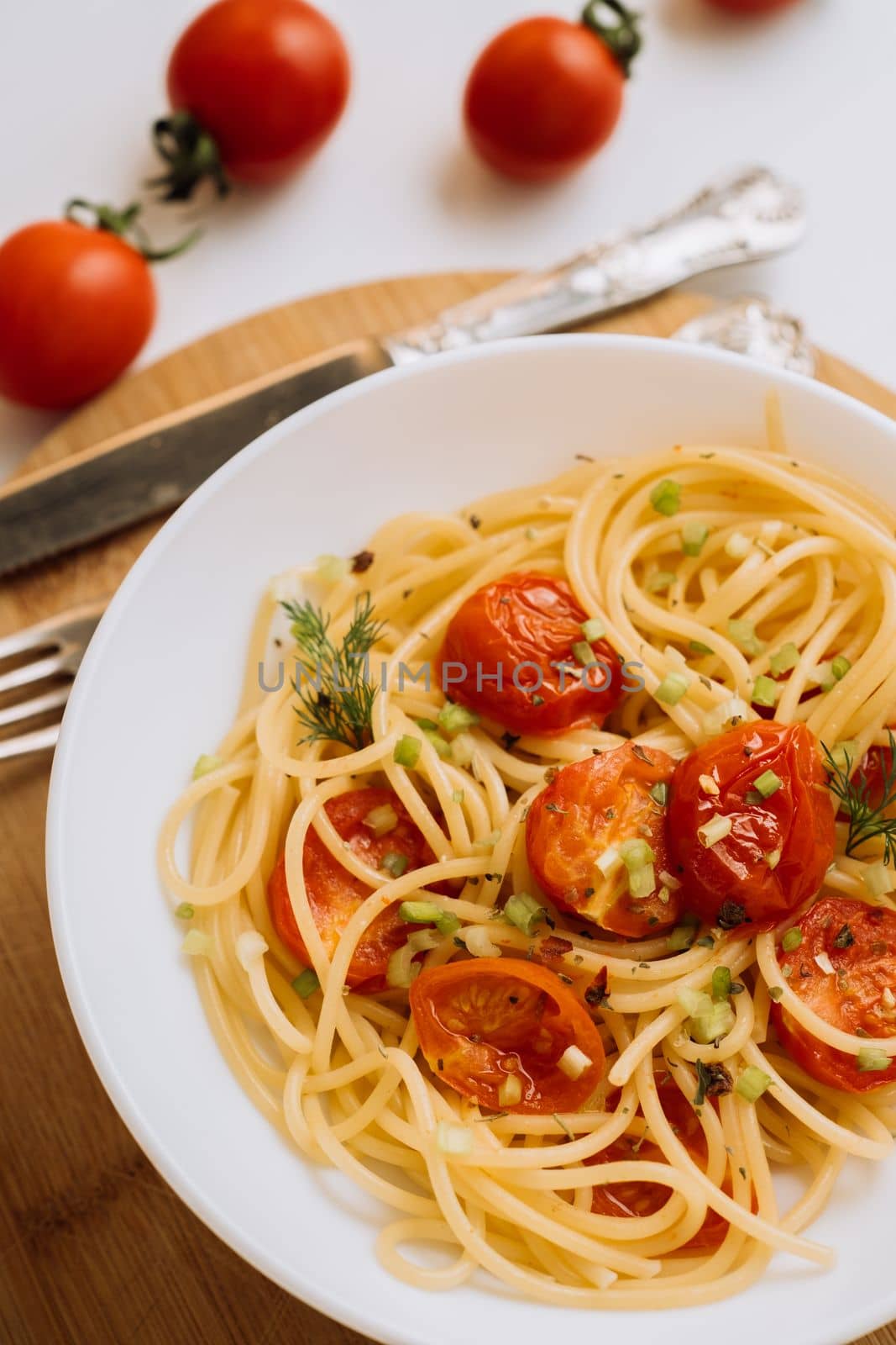 Close up portion of spaghetti pasta with cherry tomatoes sprinkled with spices in a plate on a wooden board by Romvy