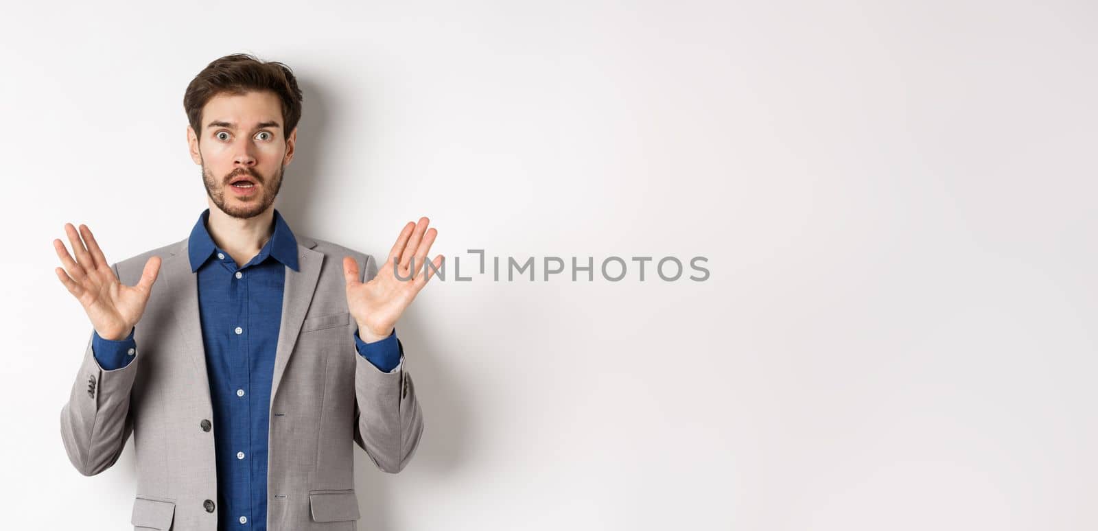 Surprised businessman in suit raising hands up and look excited, standing against white background by Benzoix
