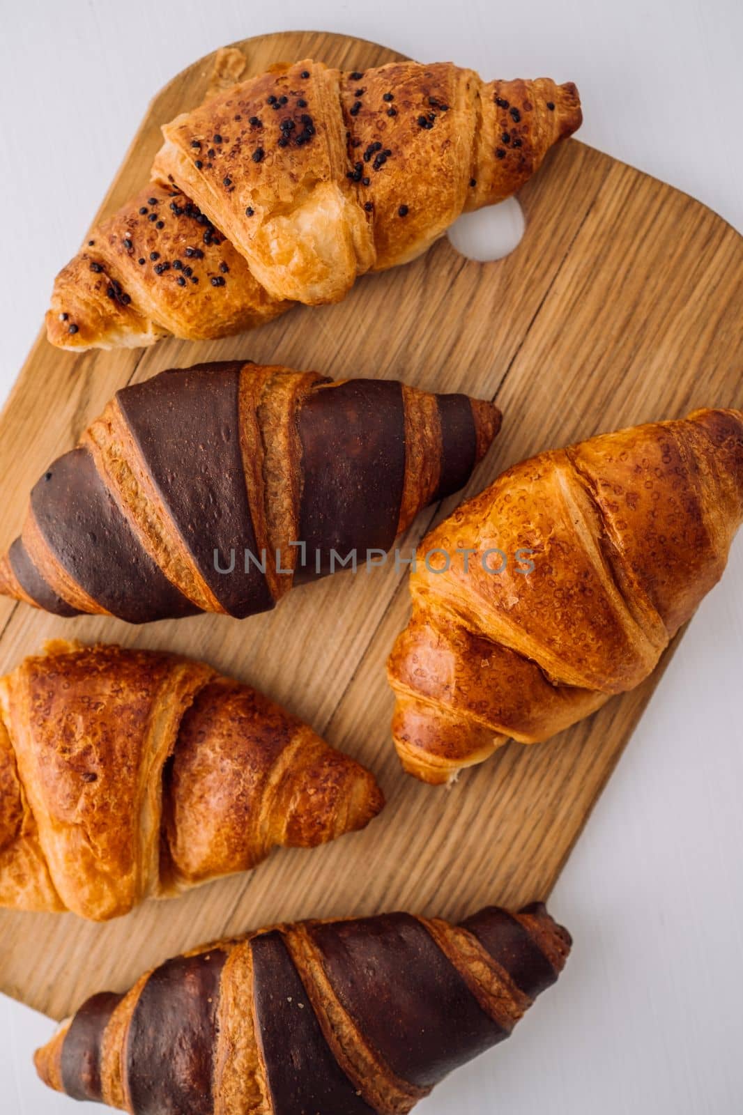 Flat lay of bunch of appetizing brown and chocolate croissants on wooden board on white table