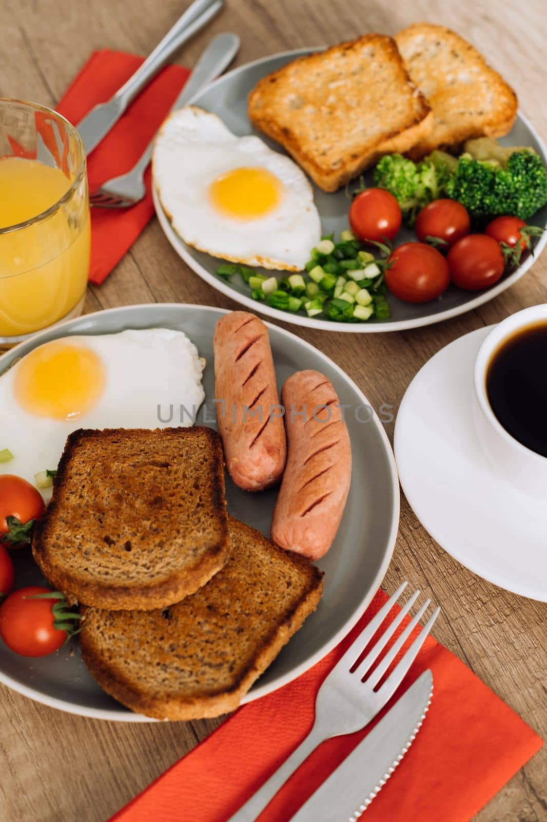 English breakfast with cup of black coffee and orange juice, grilled sausage and whole wheat toast with fried egg and cherry tomatoes on plate