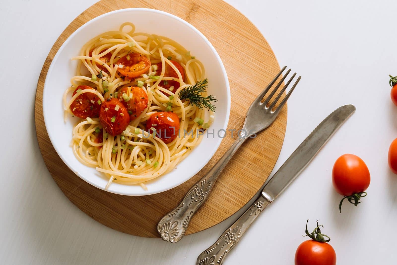 Flat lay portion of spaghetti pasta with cherry tomatoes sprinkled with spices in a plate on wooden board