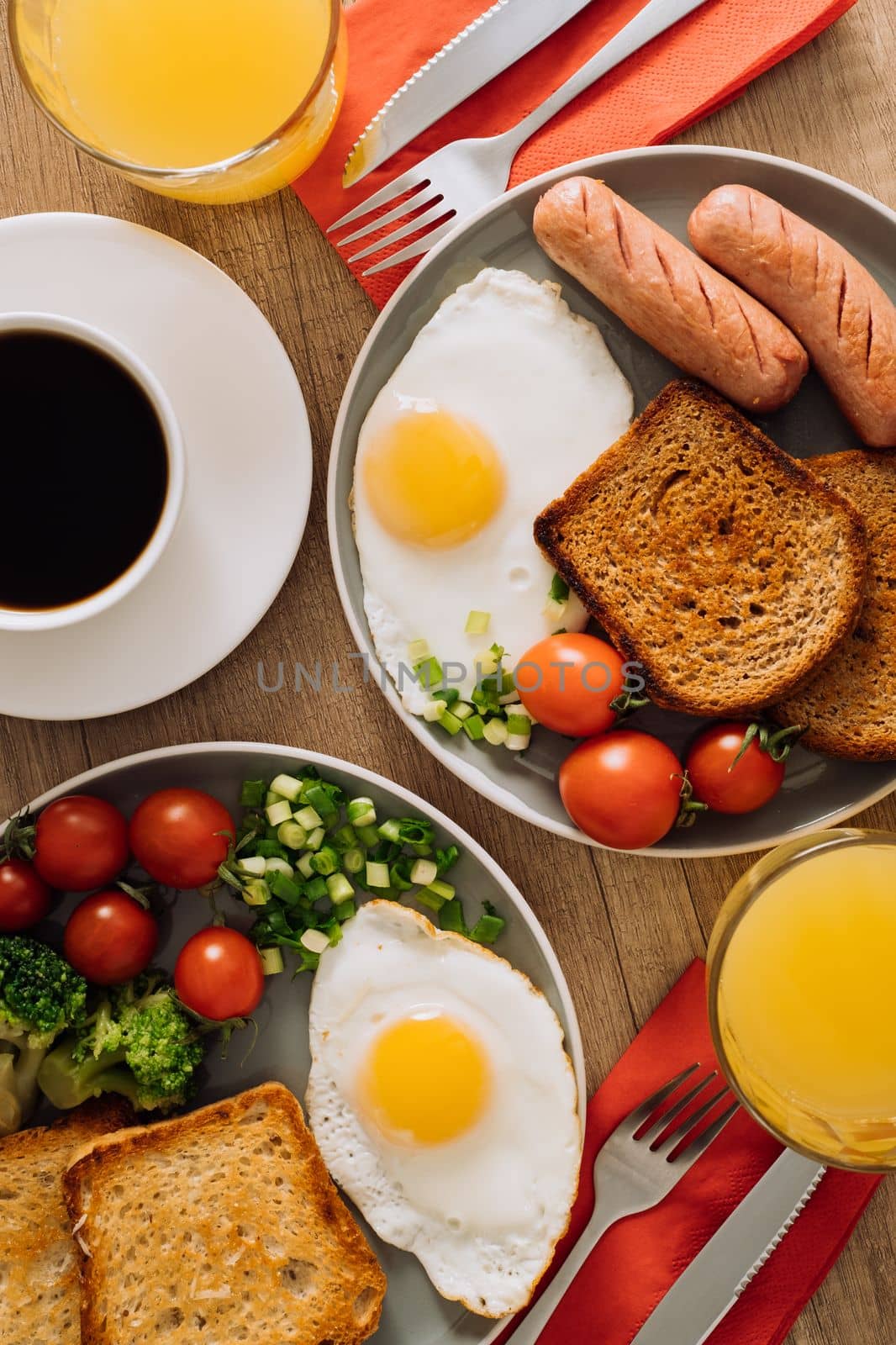 Flat lay of English breakfast with cup of black coffee and orange juice, grilled sausage and whole wheat toast with fried egg and cherry tomatoes