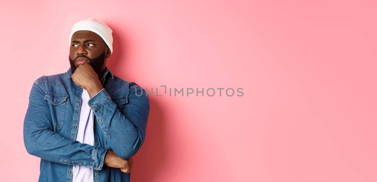 Serious thoughtful african american male model making decision, looking left concerned, thinking or having doubts, standing over pink background by Benzoix