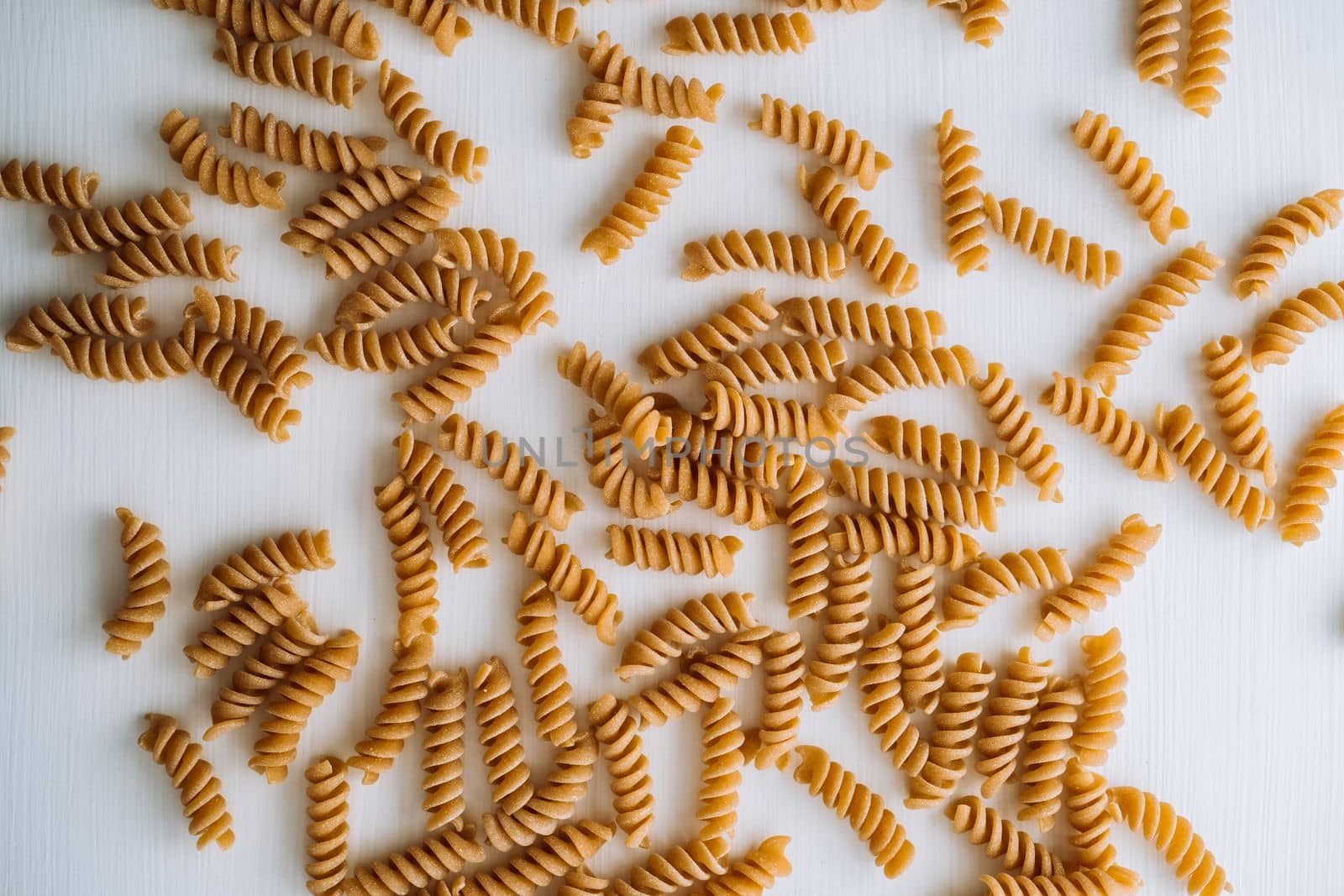 Flat lay of scattered many wavy pasta from whole wheat flour on the white table