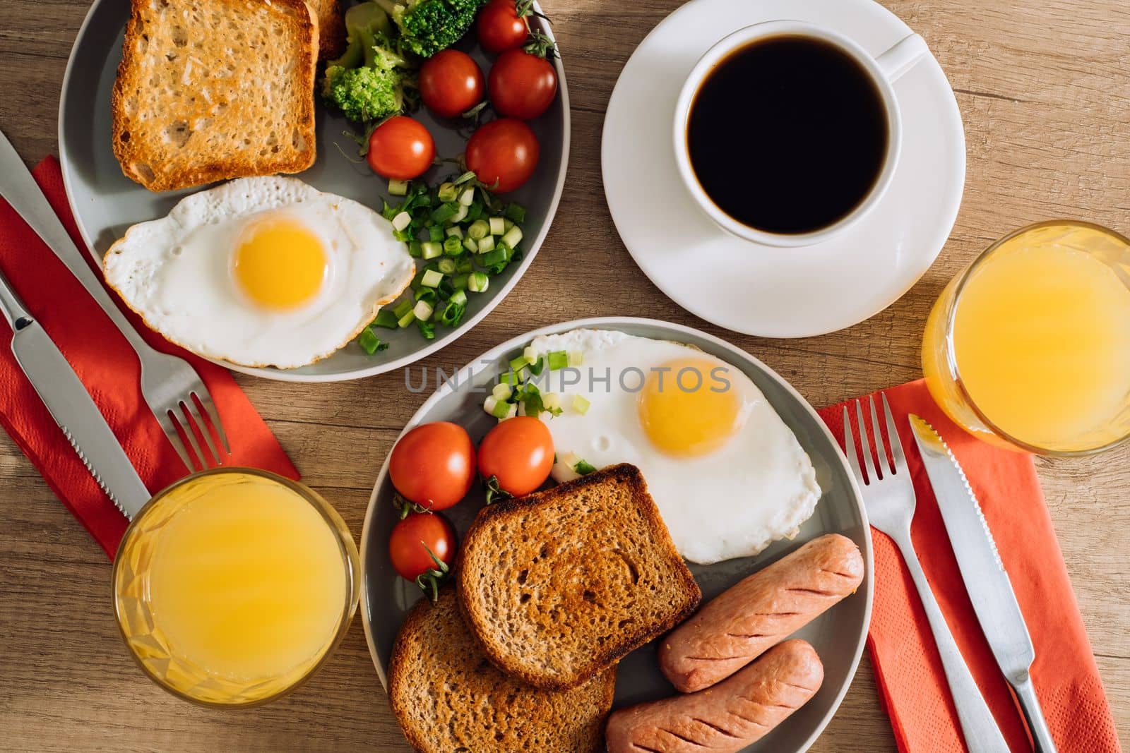 Flat lay English breakfast with cup of black coffee and orange juice, grilled sausage and whole wheat toast with fried egg and cherry tomatoes by Romvy