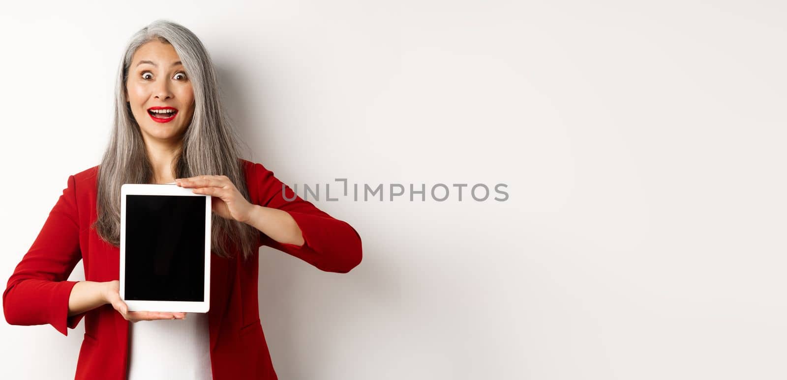 Business. Surprised asian female manager showing blank digital tablet screen, raising eyebrows and gasping fascinated, standing over white background.