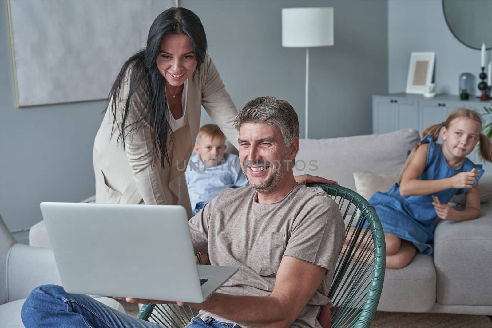 mom and dad use laptop while their kids relax on the couch by asdf