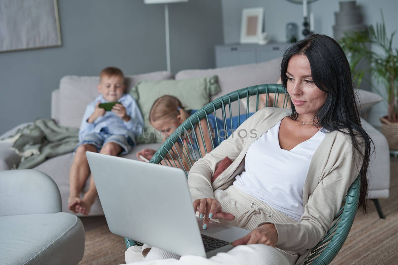 woman using laptop with interest at home while child relax on sofa by asdf