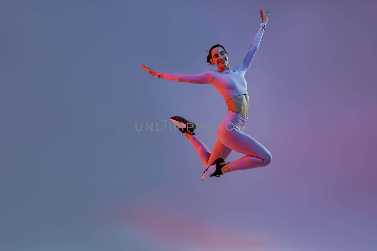 Smiling sporty woman in sportswear jumping on studio background. Sport and healthy lifestyle by Yaroslav_astakhov