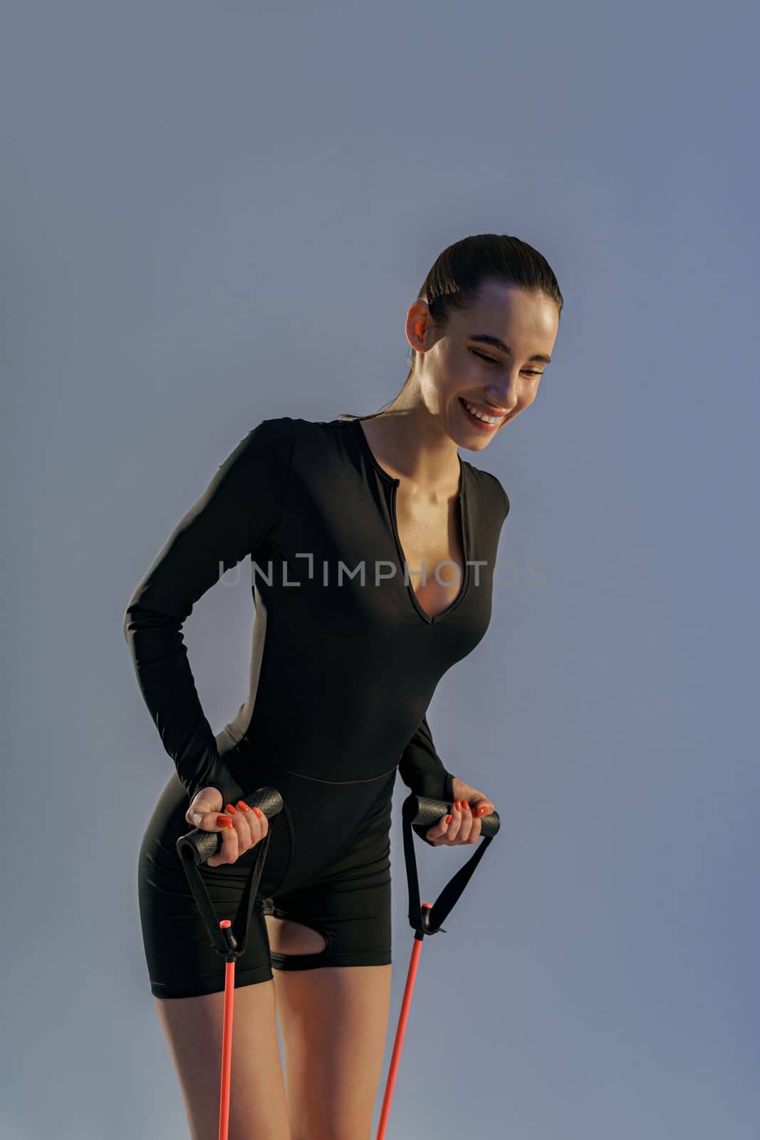 Close up of smiling woman performs fitness exercises with resistance band on studio background by Yaroslav_astakhov
