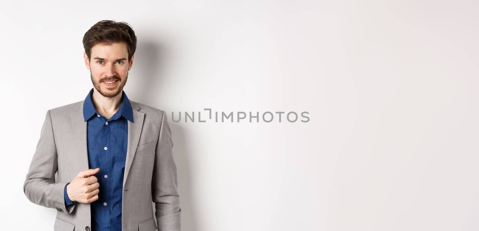 Confident businessman in suit smiling at camera, standing self-assured against white background.