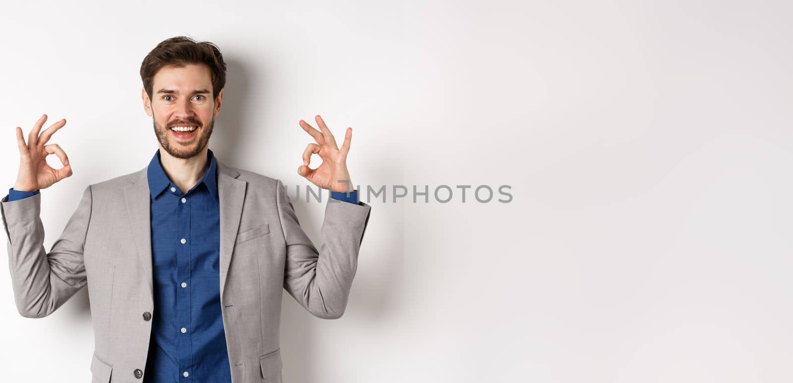 Good choice. Smiling businessman in suit showing okay signs and look happy, recommending good deal, like and approve your choice, standing satisfied on white background by Benzoix