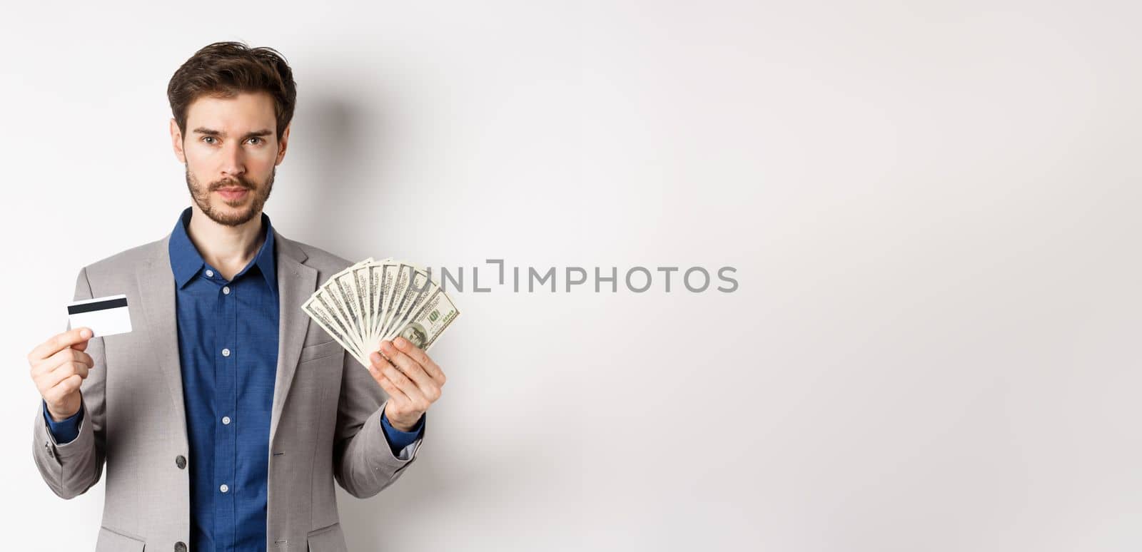 Successful businessman making money, standing in suit with dollar bills and plastic credit card, white background.